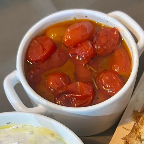 Ramekin branco cheio de tomates cereja confitados, brilhantes, imersos no azeite temperado